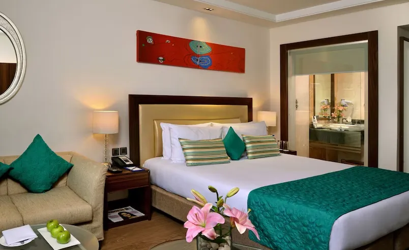 Club room at Golden Tulip Lucknow showing neatly made bed, side tables, and warm interior lighting