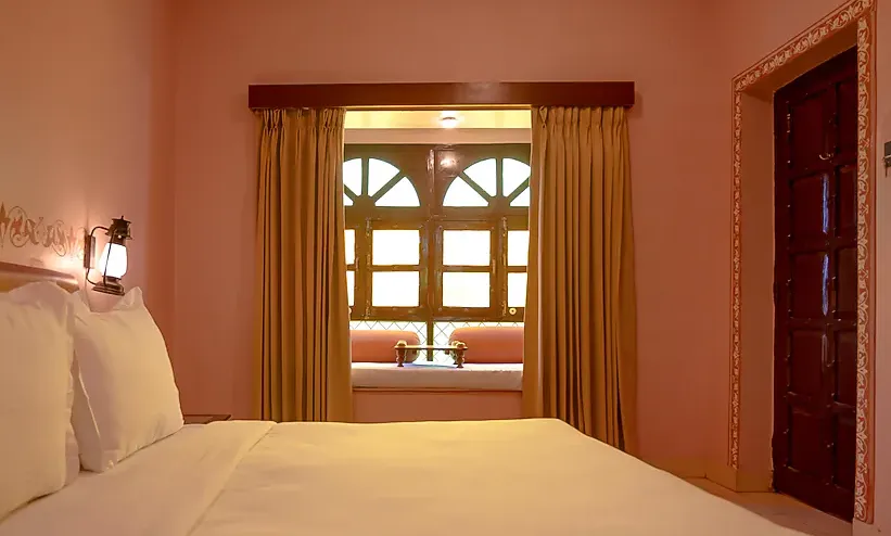 Deluxe room at Hotel Nirali Dhani Jodhpur showing spacious sleeping area and window view