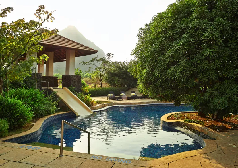 Swimming pool at Club Mahindra Resort - Tungi Lonavala with clear water and deck chairs