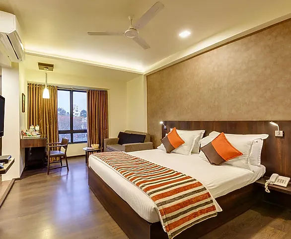 Deluxe room interior at Regenta Place Raysons Kolhapur with modern bed and seating area